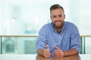 smiling-man-sitting-cafe-table-gesturing-min smiling-man-sitting-cafe-table-gesturing-min